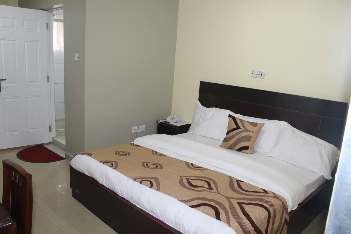 Una habitación de hotel con una cama, una mesita de noche, un teléfono y una puerta.