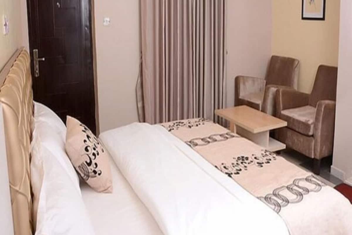 Habitación de hotel con cama, dos sillas, una mesita, aire acondicionado y una puerta.
