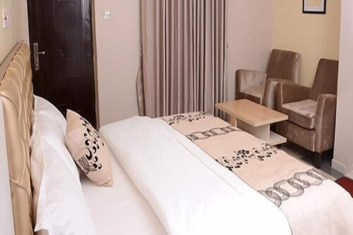 Una habitación de hotel con una cama, dos sillas, una mesita, una puerta y un equipo de aire acondicionado.