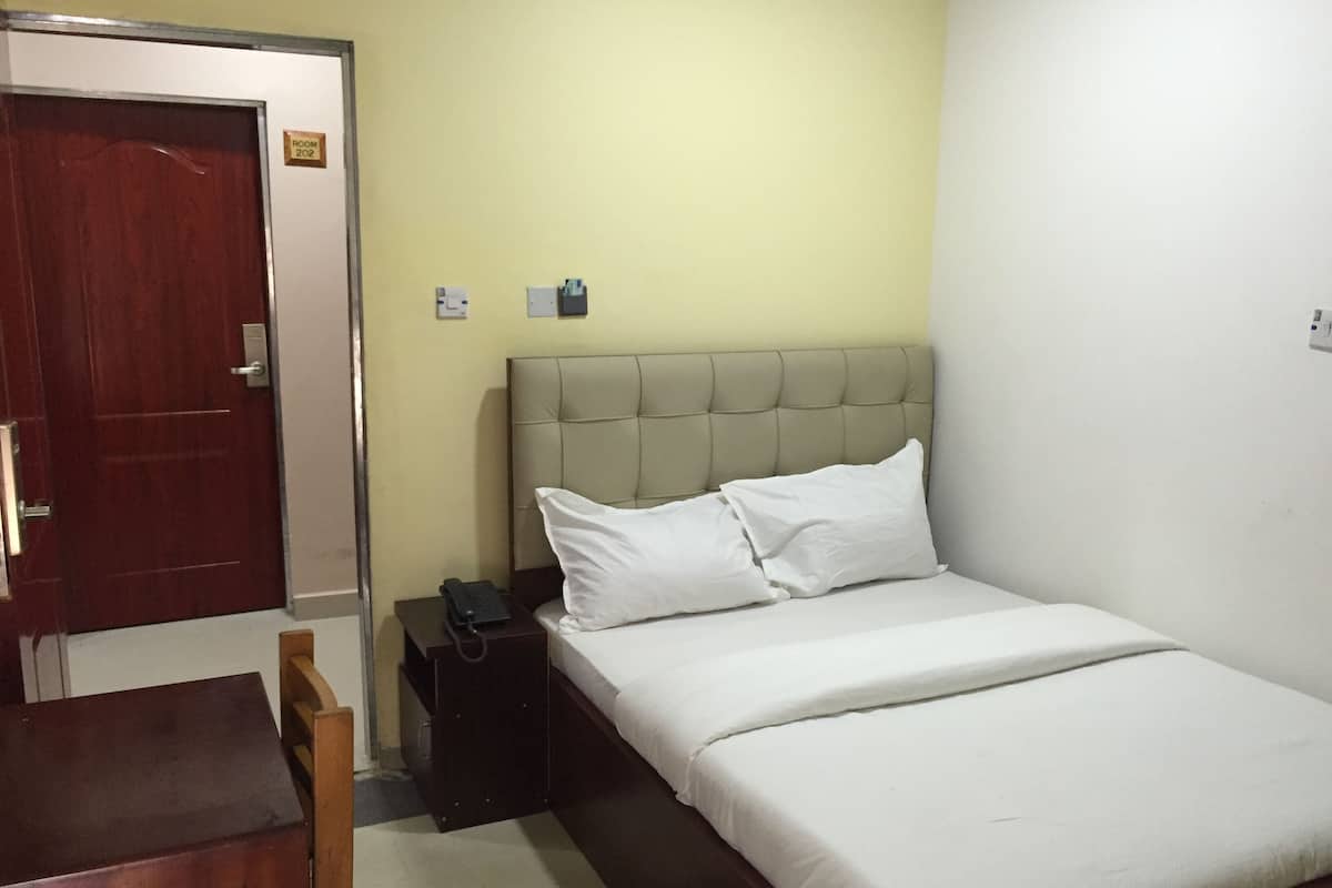 Habitación de hotel con cama, teléfono en la mesita de noche, mesita, puerta y letrero con el número de habitación.