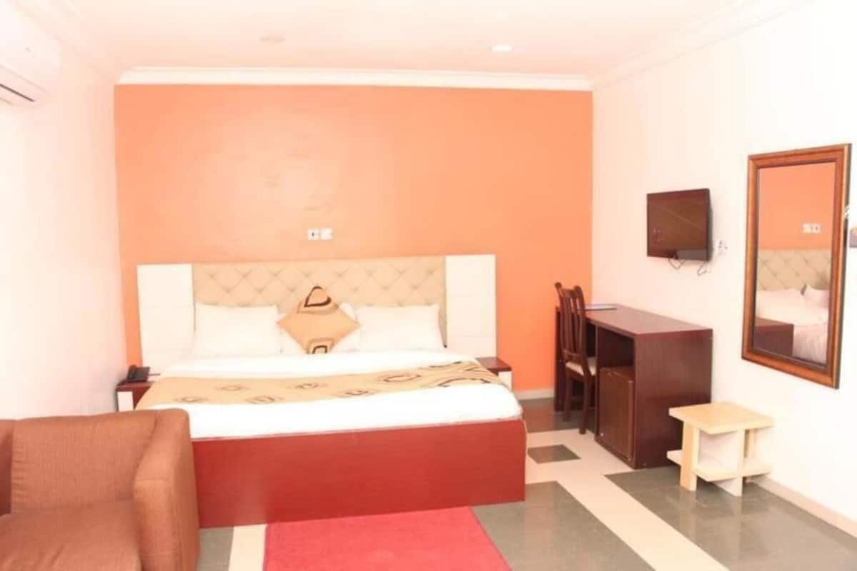 Un dormitorio con cama, escritorio, silla, una mesita y un espejo en la pared.