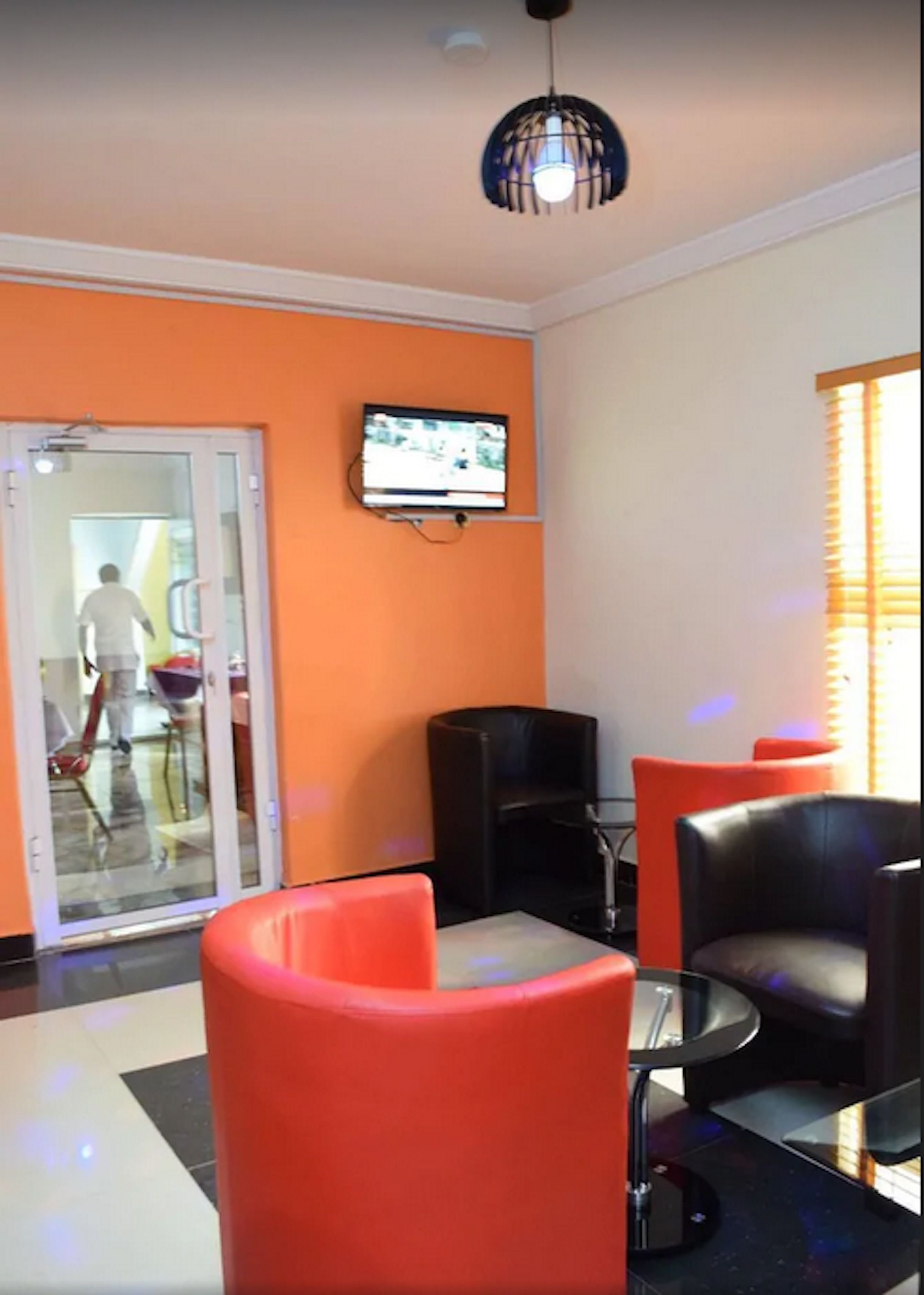 A room with orange walls, a television mounted on the wall, and several black and red chairs.