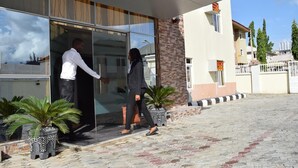 A modern building with a glass entrance, potted plants, and a paved walkway. - Chariot Hotel (Abuja)