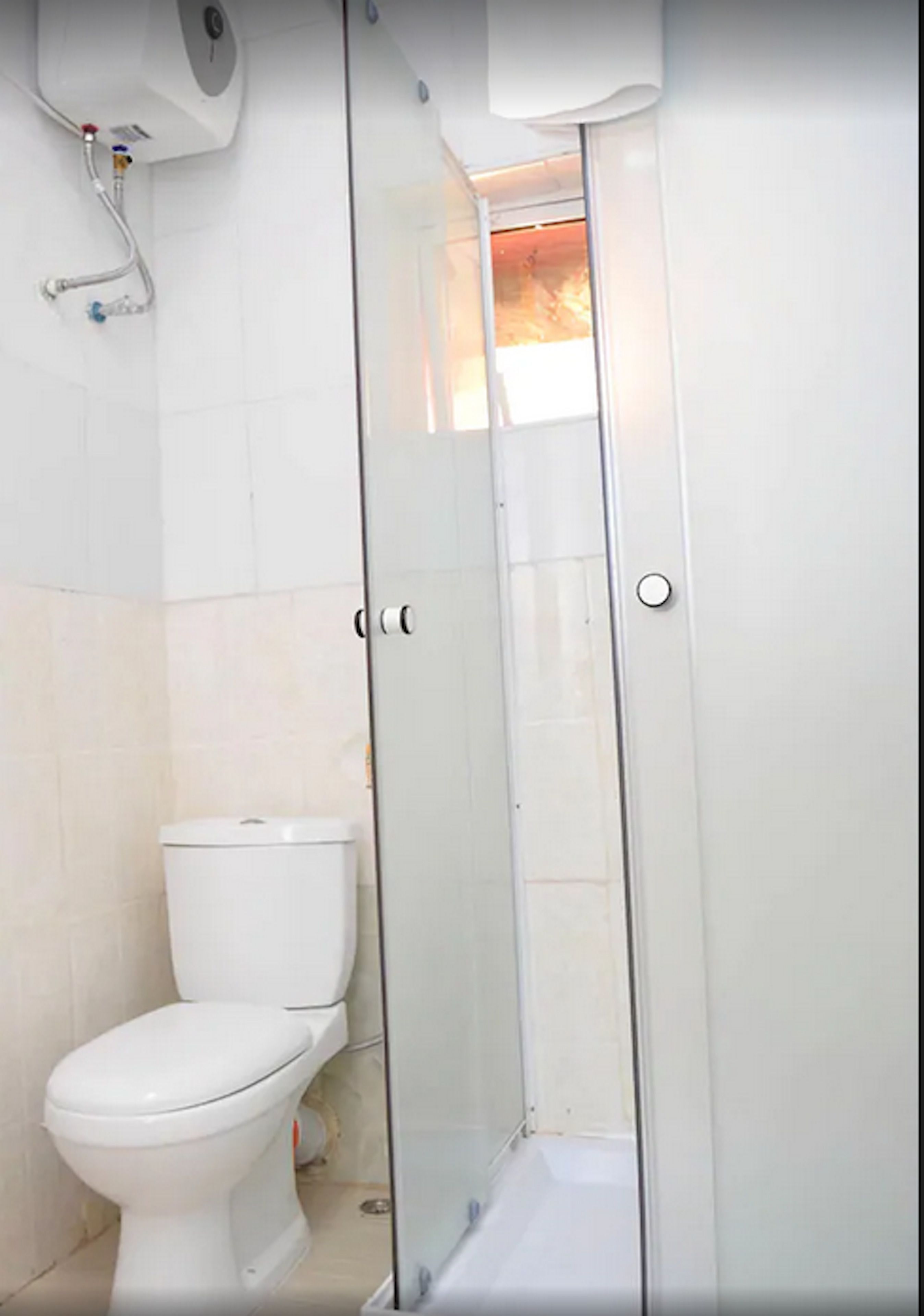 A bathroom with a toilet, a glass shower enclosure, and a white tiled wall.