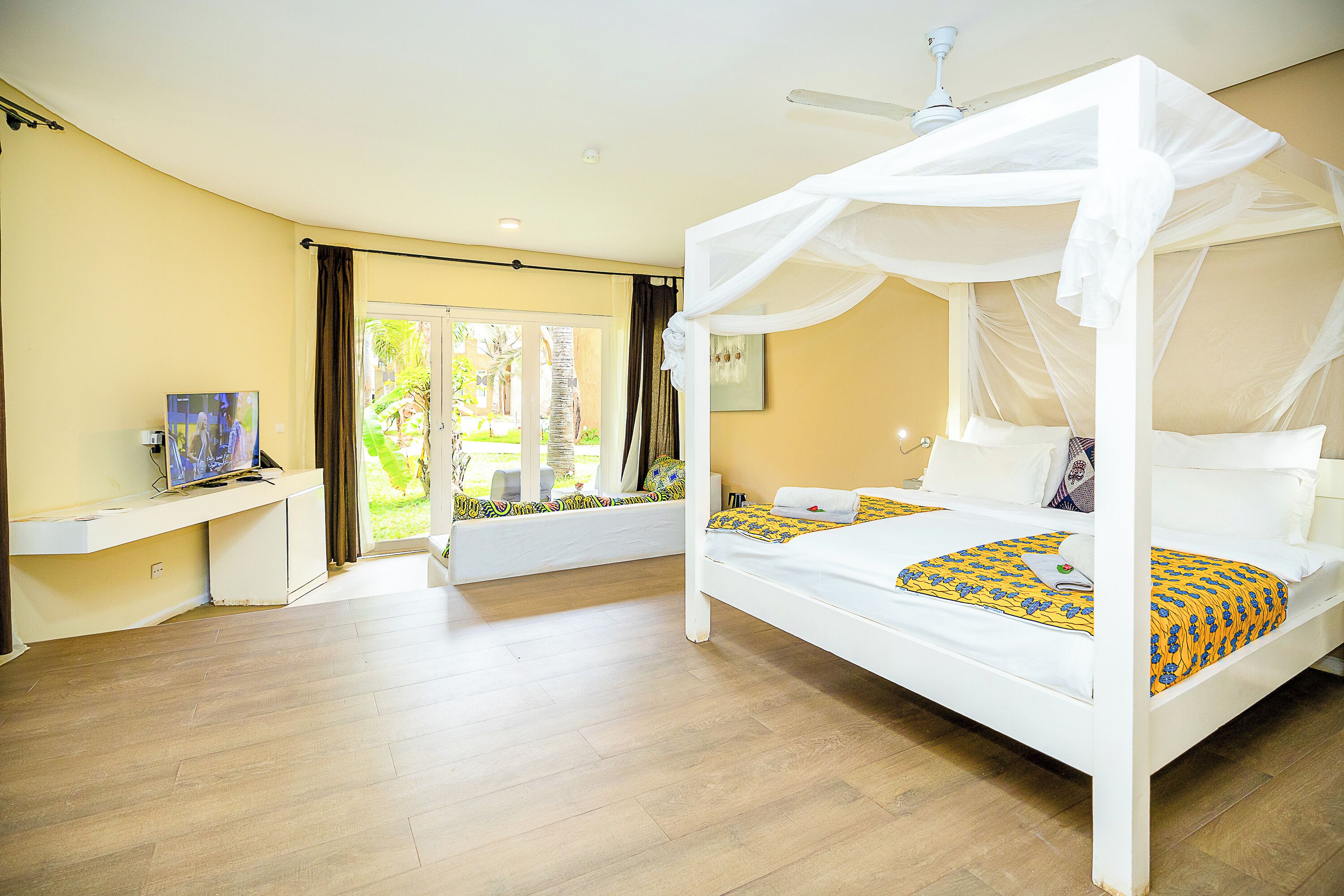 A bedroom with a canopy bed, a desk with a TV, and a view of the outdoors.