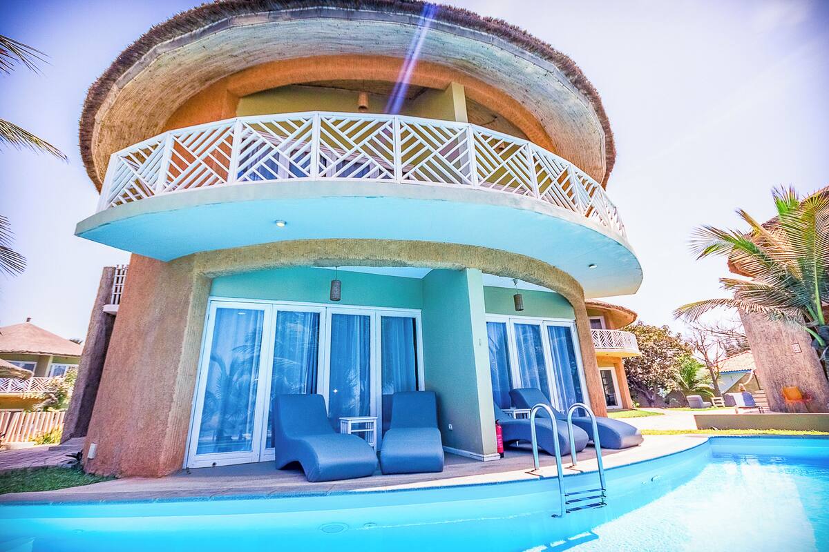 Ein Hotel mit Pool, Liegestühlen und einem Balkon mit Reetdach.