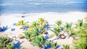 Une plage bordée de palmiers, avec une eau d’un bleu limpide et quelques personnes.