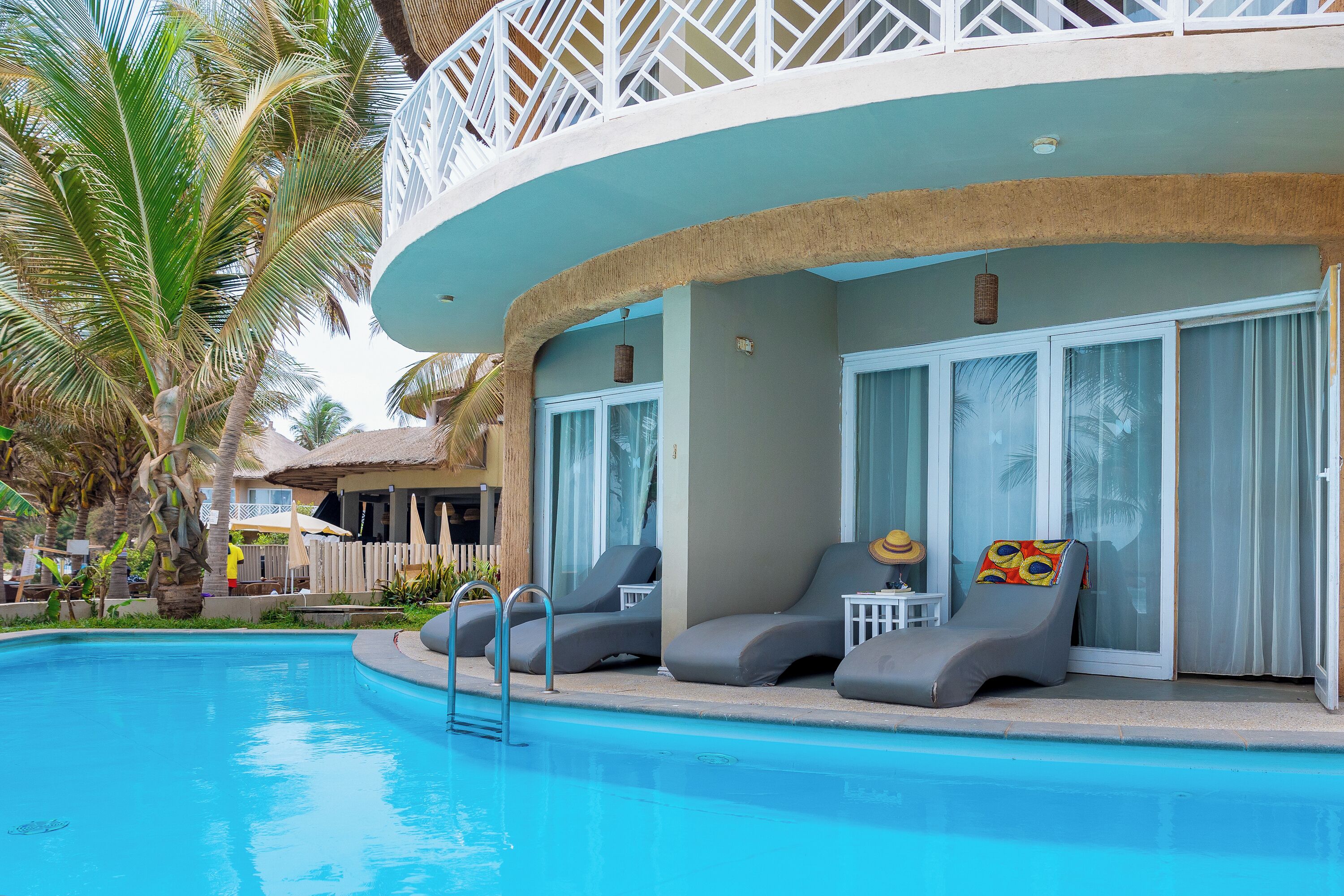 Un área de piscina con sillas de descanso, una escalera de piscina y un edificio con amplias ventanas y un balcón.