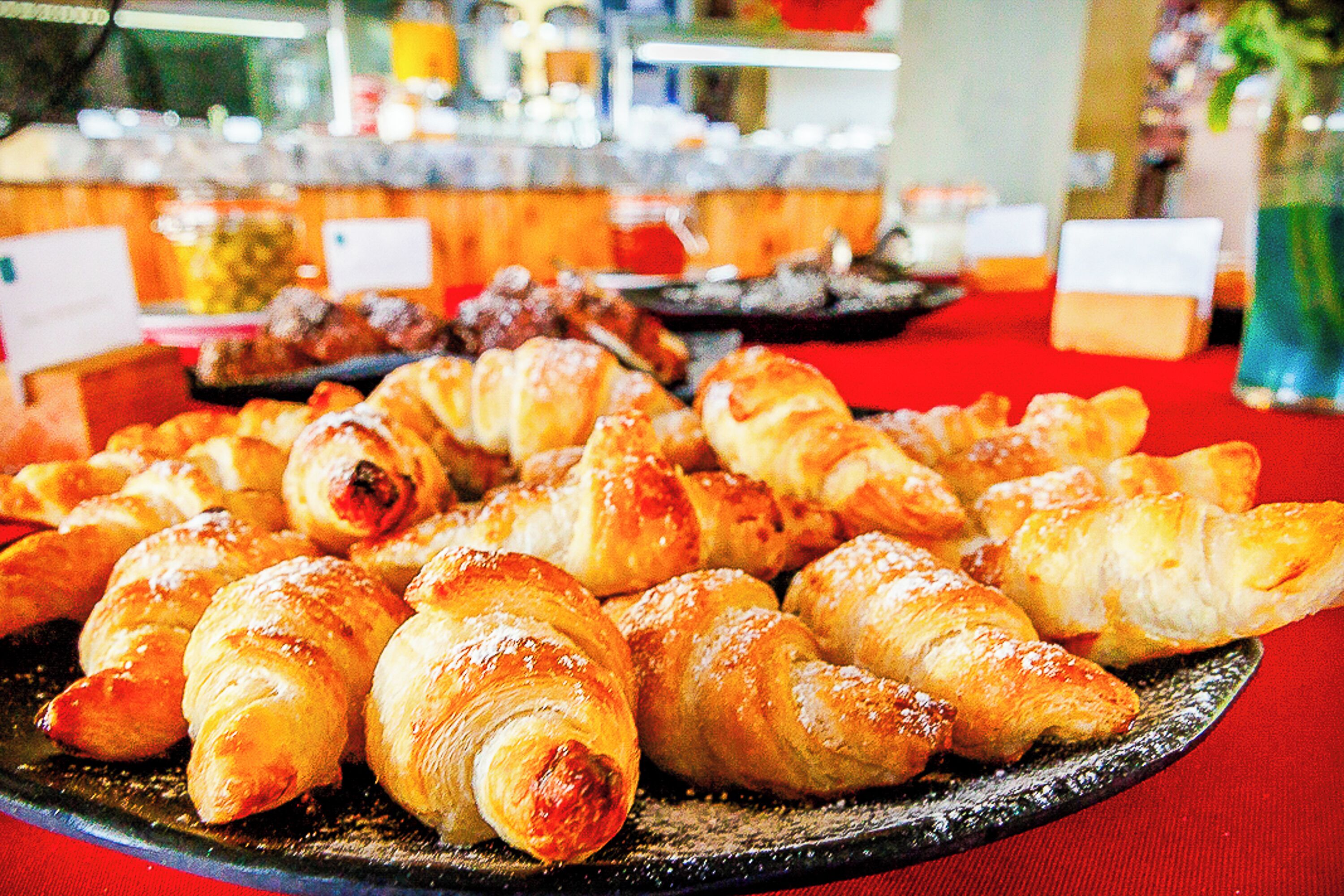 A variety of pastries on a tray, including croissants and other baked goods, displayed on a table with a red tablecloth.