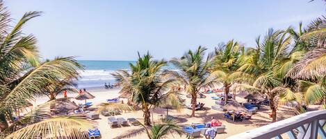 A beach with palm trees, sun loungers, and umbrellas.