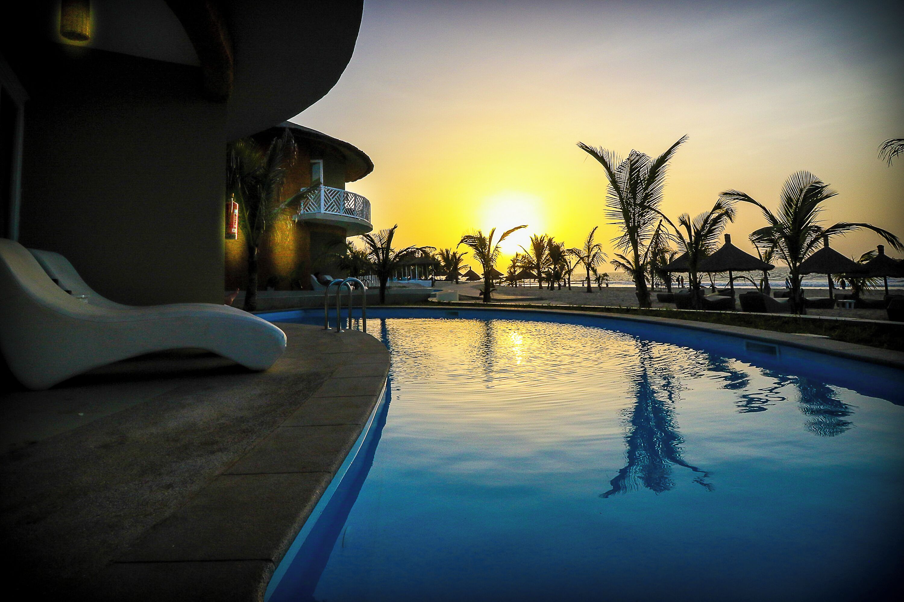 Una piscina con vistas al atardecer, sillas de descanso y palmeras.