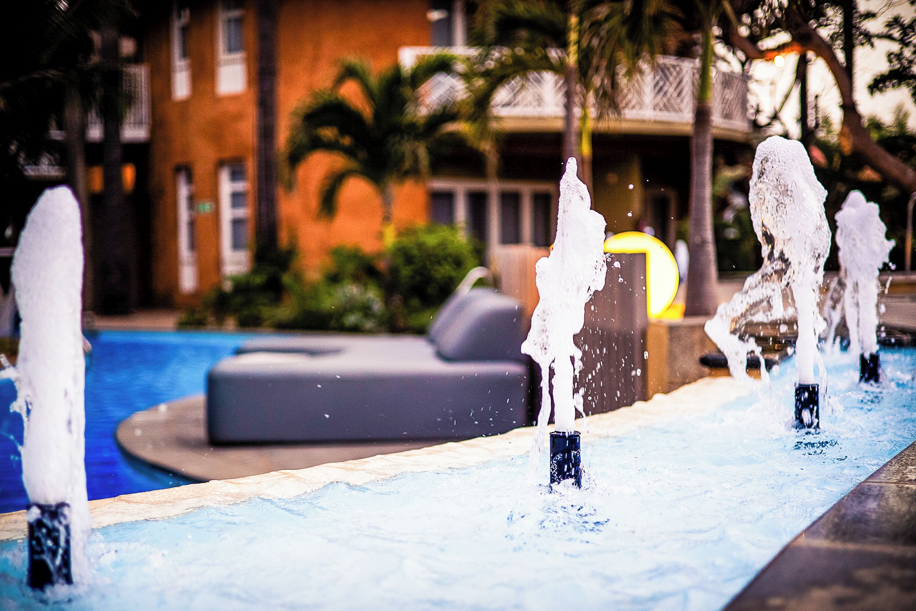 Una piscina con múltiples chorros de agua y un área de descanso al fondo.