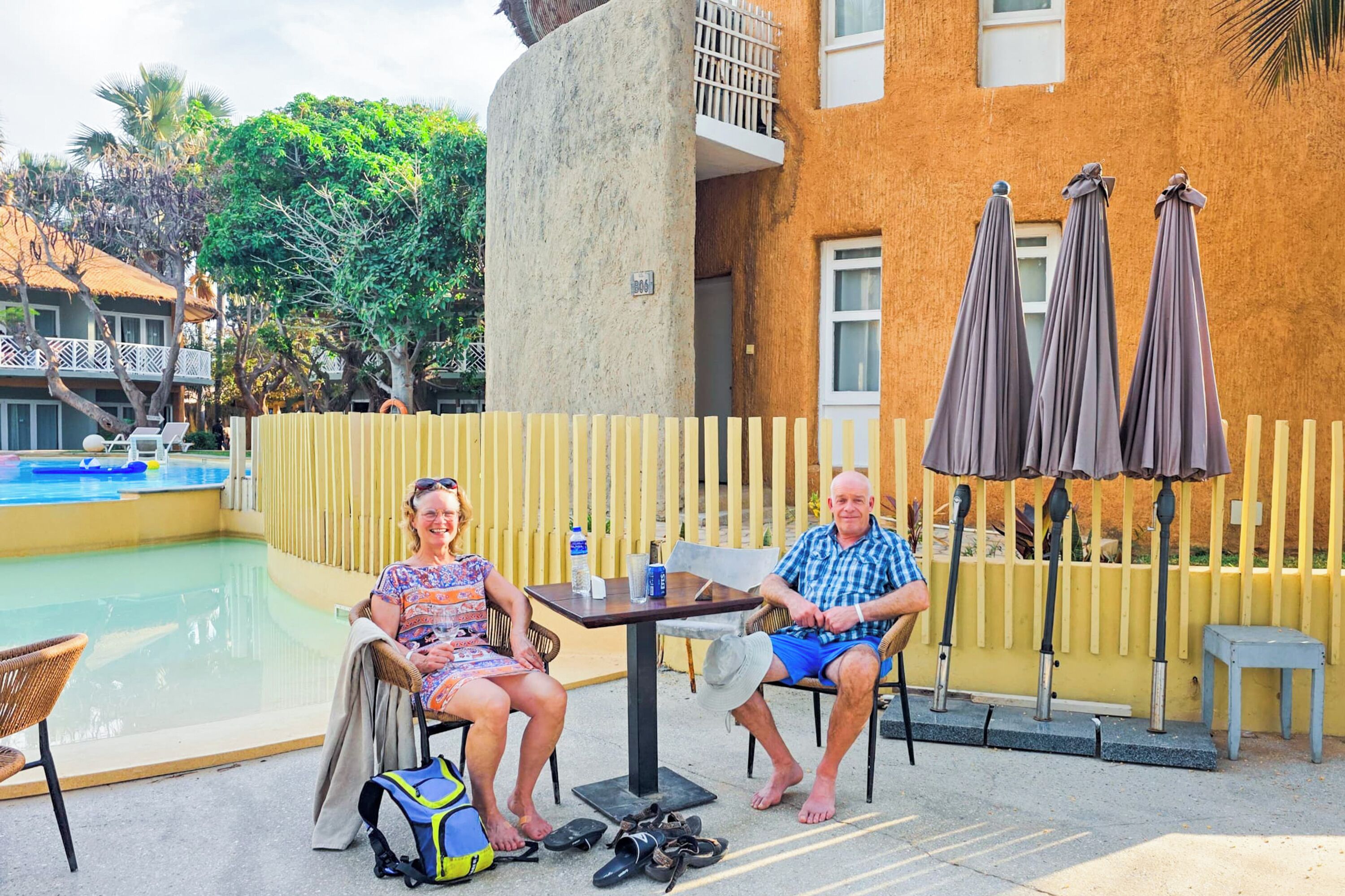 A poolside area with a table and chairs, umbrellas, and a building with a textured facade.