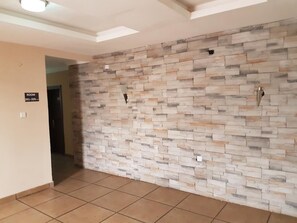 A hallway with a stone wall, a sign indicating room numbers, and a tiled floor.