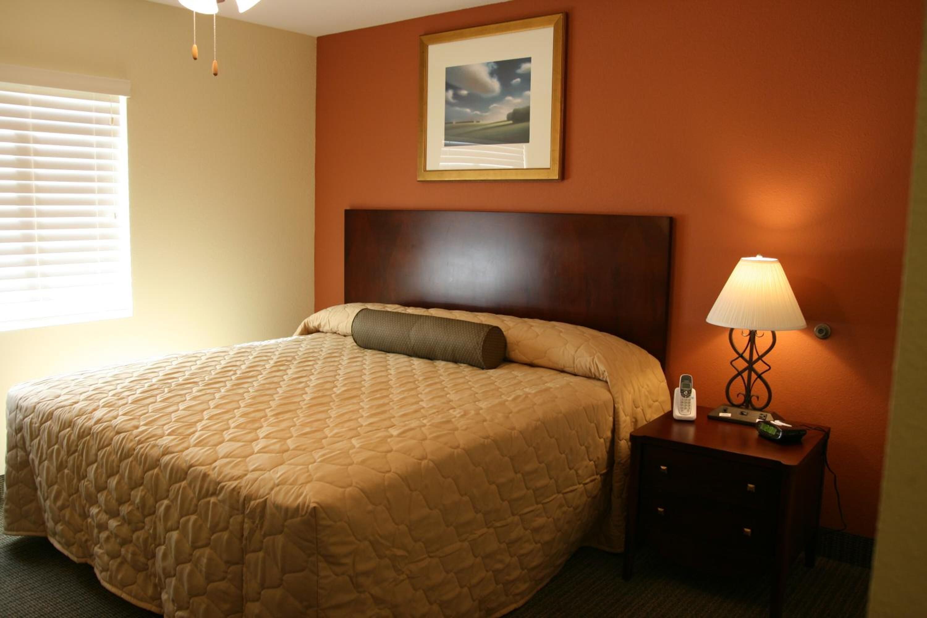 Una habitación de hotel con una cama grande, una mesita de noche con una lámpara y un cuadro enmarcado en la pared.