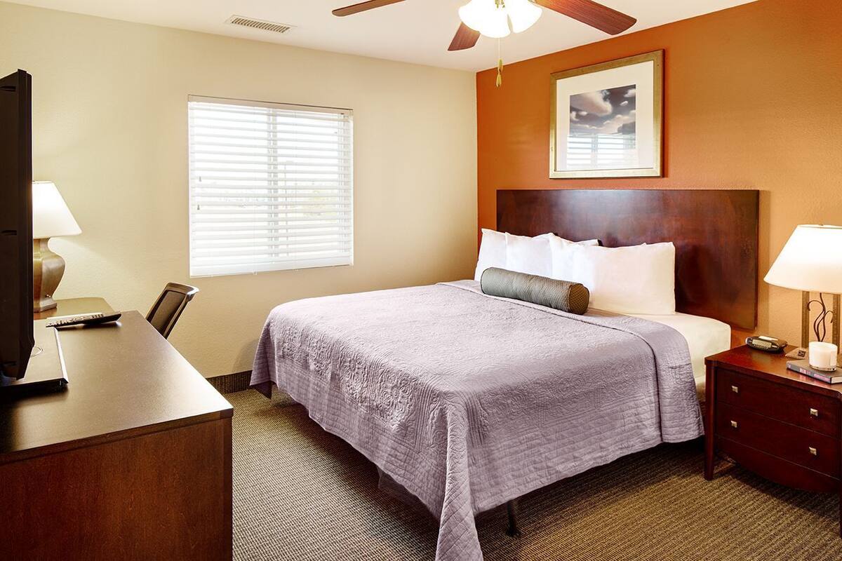 A hotel room with a bed, a desk, a television, and a window with blinds.
