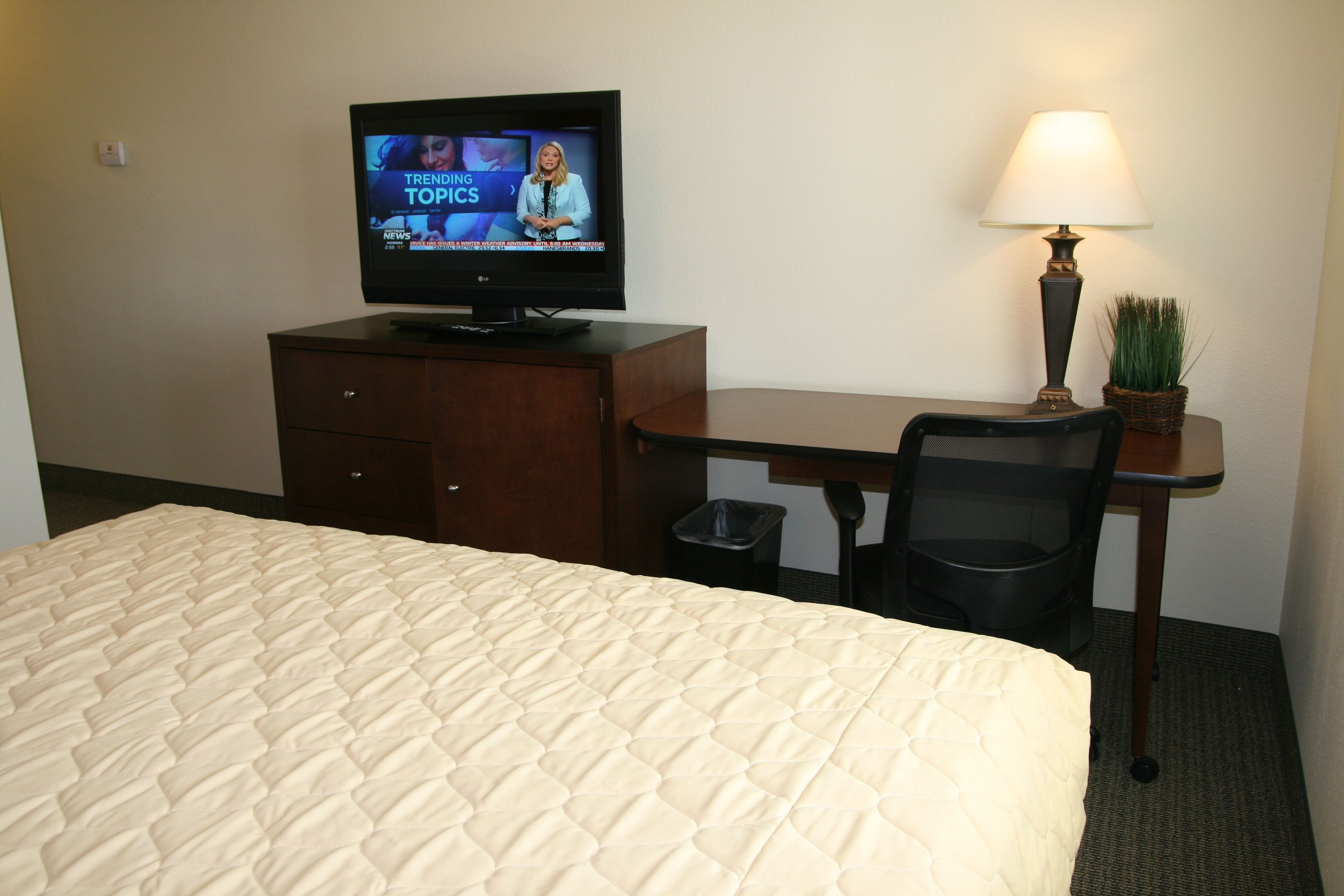 A hotel room with a bed, a desk, a television, a lamp, and a trash bin.