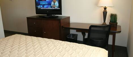 A hotel room with a bed, a desk, a television, a lamp, and a trash bin.