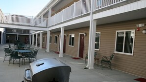 Un motel con patio cubierto, mobiliario exterior y una parrilla.