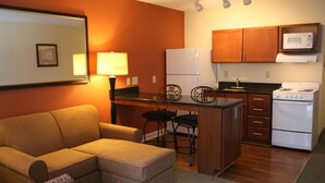 Un espacio habitable pequeño con sofá, una cocina compacta que incluye refrigerador, microondas y estufa, y una zona de comedor con dos sillas.