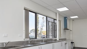 A modern kitchen with white cabinets, stainless steel countertops, and a large window with a view of the outside. - Three Palms Lodge (Auckland)
