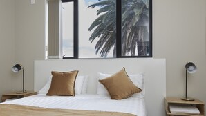 A bedroom with a large bed, two nightstands, a window with a view of palm trees, and a ceiling light. - Three Palms Lodge (Auckland)