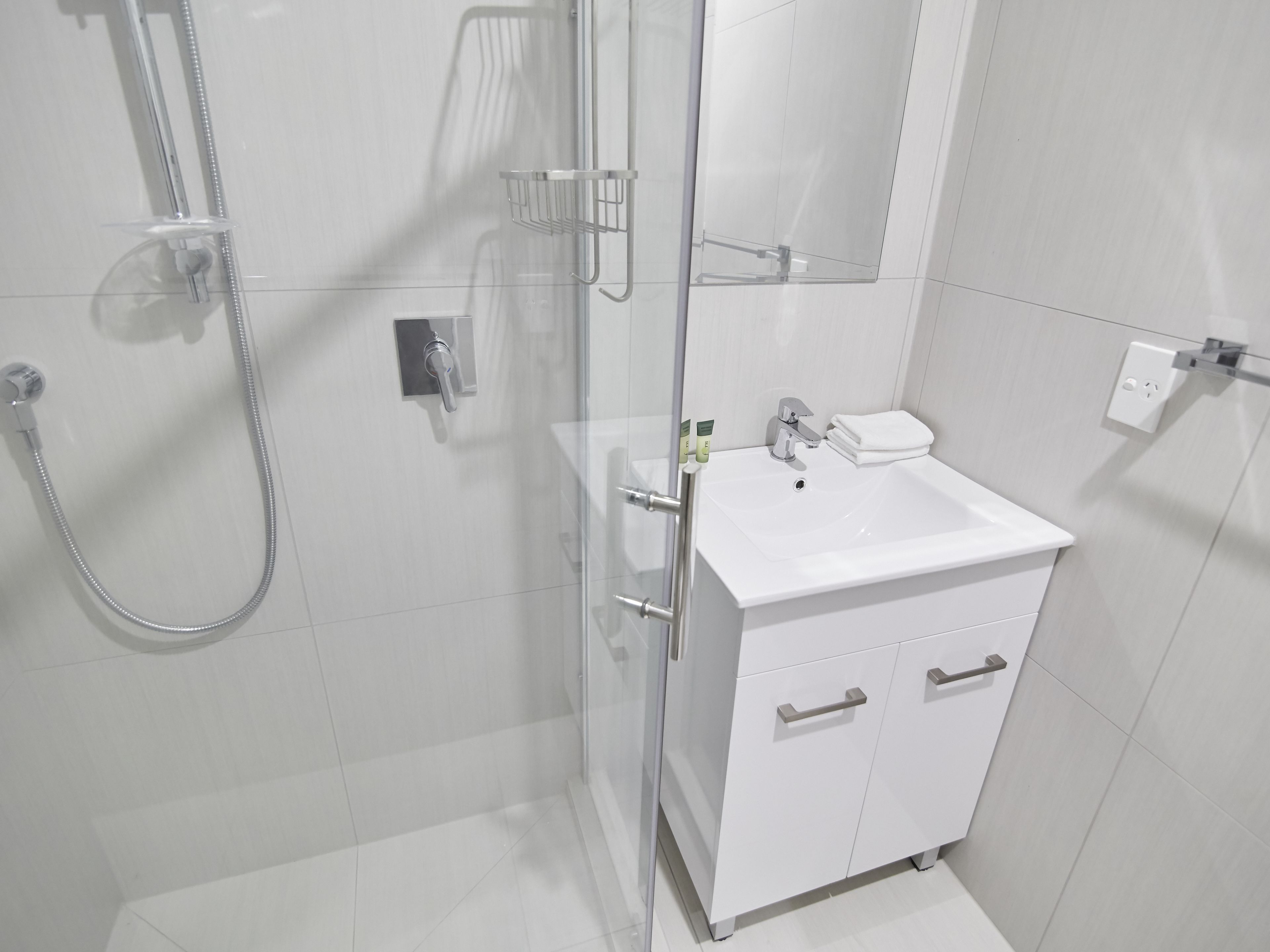 Uma casa de banho moderna com cabine de duche em vidro, uma sanita branca com espelho e um armário com gavetas.