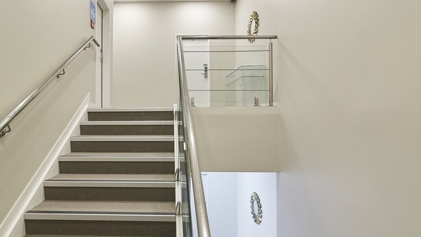A staircase with a handrail, carpeted steps, and a glass railing on the upper landing. - Three Palms Lodge (Auckland)