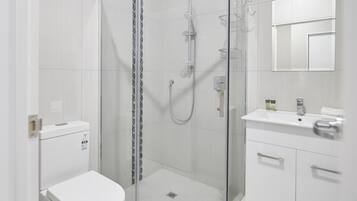 Un baño moderno con ducha de vidrio, inodoro blanco y lavamanos con espejo.
