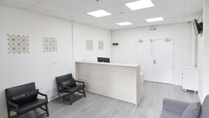 A reception area with a light-colored desk, two black chairs, a grey sofa, and a white door. - Three Palms Lodge (Auckland)