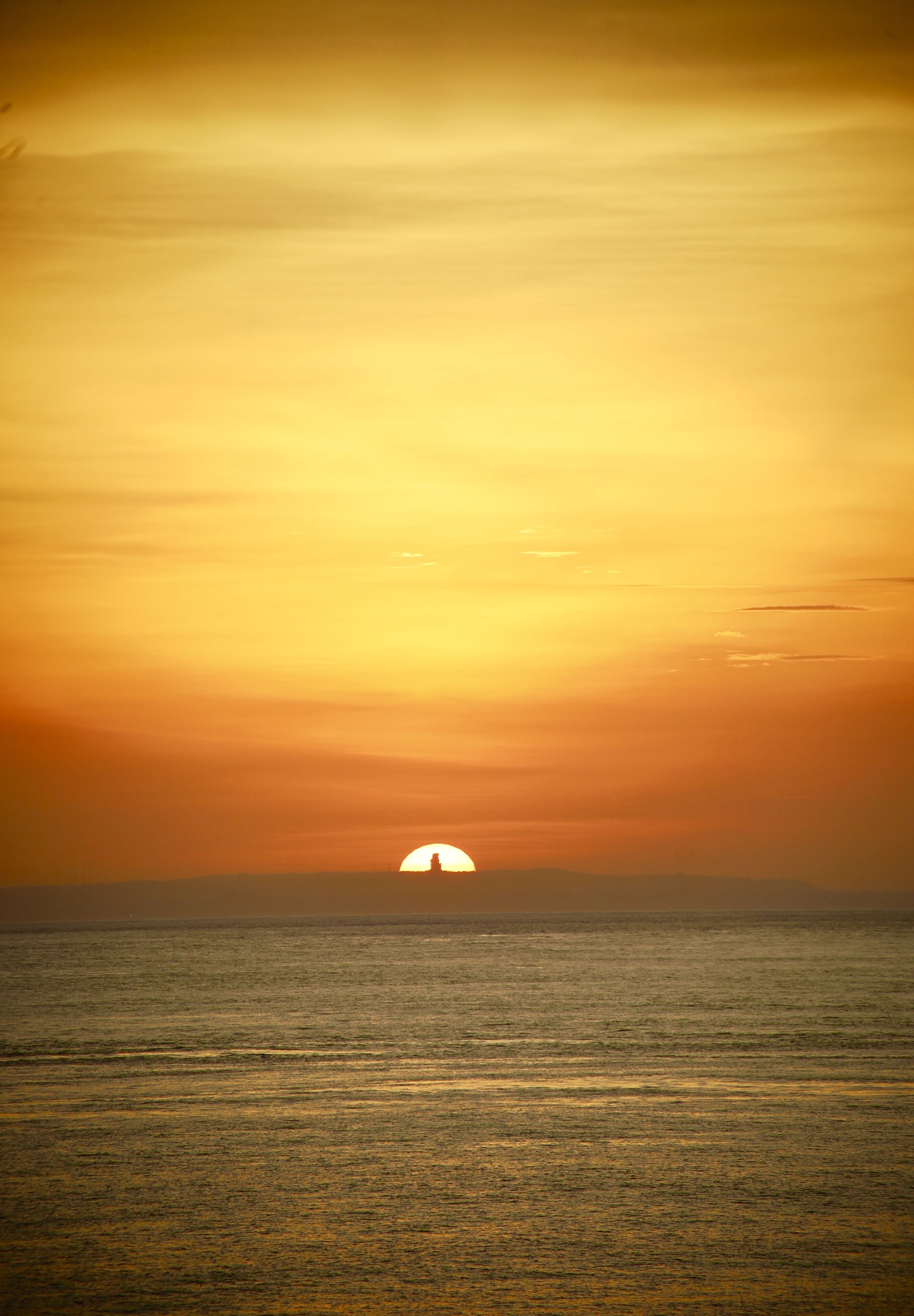 Un atardecer sobre un mar tranquilo con la silueta de una persona de pie en la orilla.