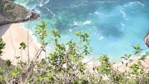 A coastal landscape with a beach, clear blue waters, and rocky cliffs. - The Palms Ceningan Hotel (Ceningan Island)