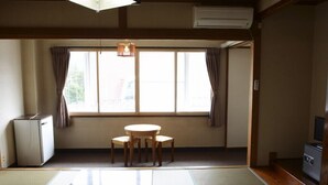 Quarto com esteiras de tatame, uma pequena mesa com cadeiras, um refrigerador e uma televisão em um armário de madeira.