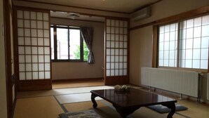 Um quarto japonês tradicional com tatames, uma mesa de madeira baixa, portas deslizantes shoji e vista pela janela com cortina.