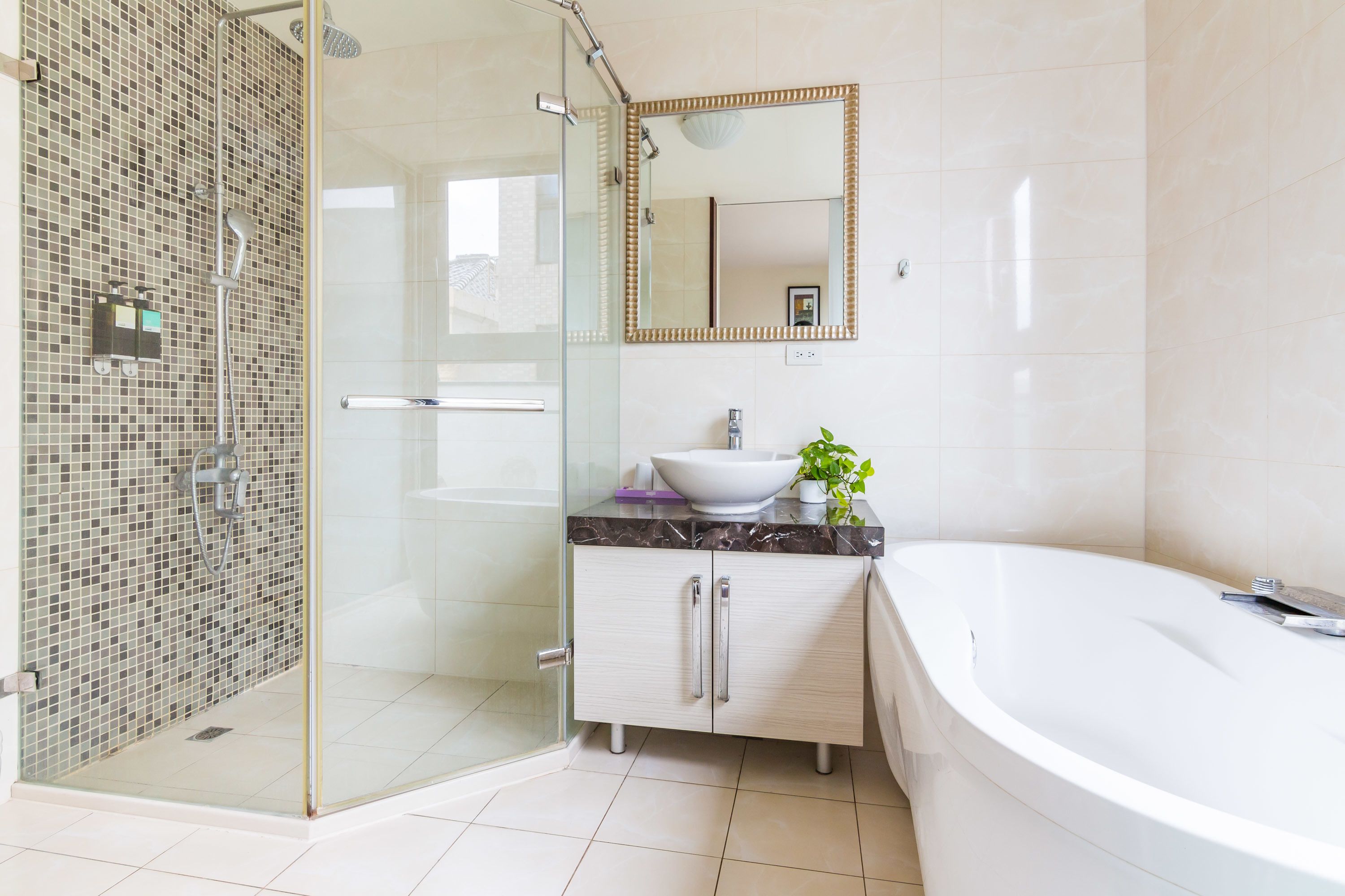 Un baño moderno con ducha envuelta en vidrio, un lavamanos blanco sobre encimera de mármol y una bañera grande.