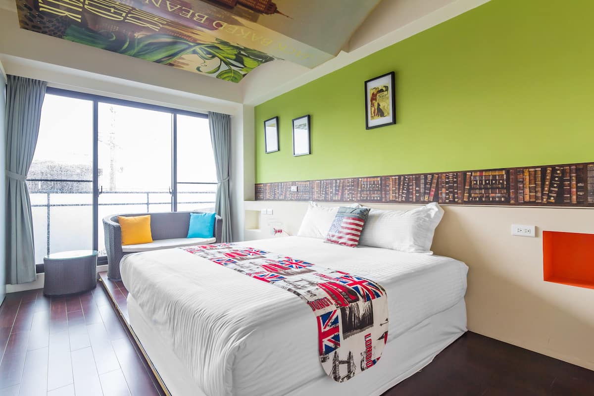 A hotel room with a large bed, a green accent wall, and a view through the window.