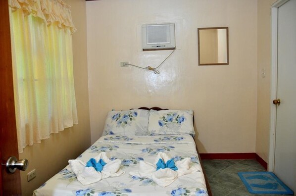 Un dormitorio con cama, ventana con cortinas, unidad de aire acondicionado, espejo y puerta.
