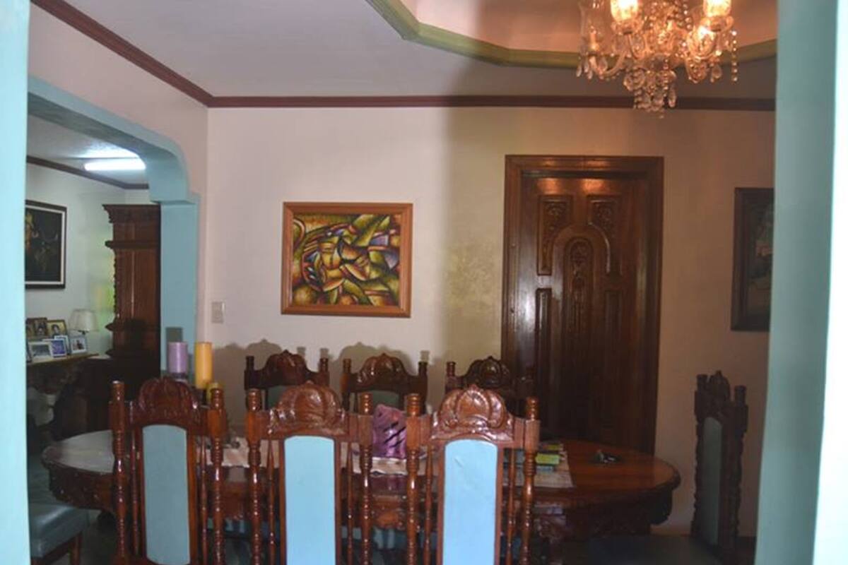 Un comedor con una mesa y sillas de madera, una araña y un cuadro en la pared.
