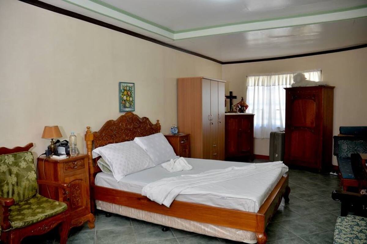 Un dormitorio con una cama de madera, una mesita de noche, una silla, un armario y una ventana con cortinas.