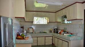 Una cocina con armarios blancos, un refrigerador y un ventanal con vistas a árboles.