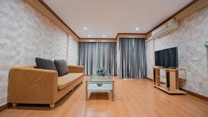 Un salon moderne avec un canapé, une table basse, un téléviseur posé sur un meuble en bois et une grande fenêtre avec des rideaux.