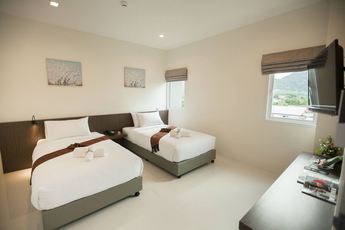 A hotel room with two beds, a desk, and a TV.