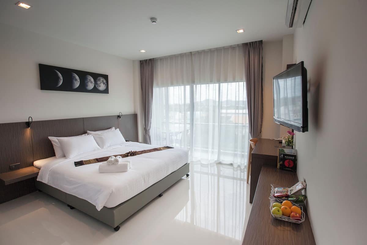 A modern hotel room with a large bed, a flat-screen TV, a bedside table, and a window with sheer curtains.
