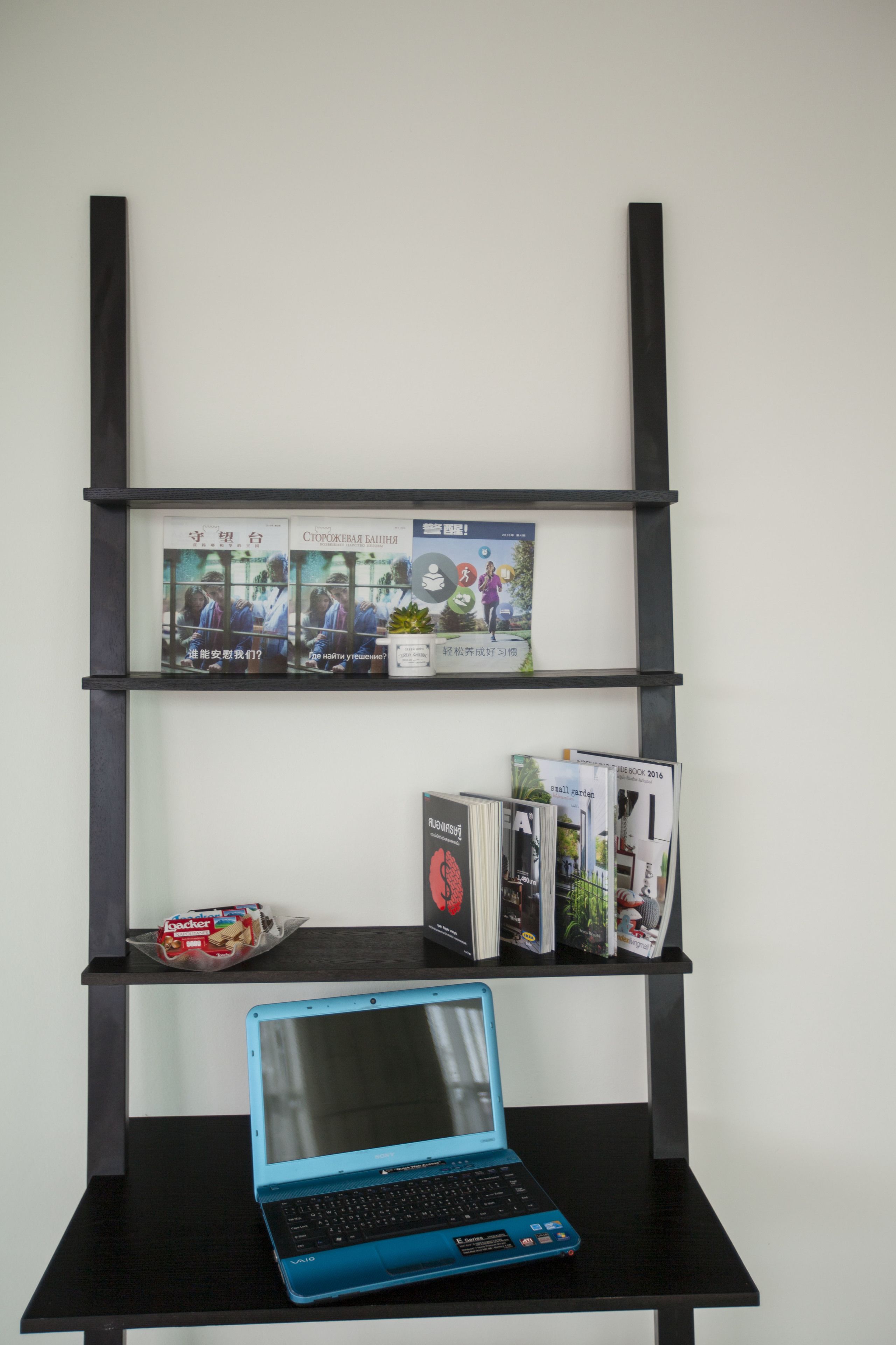 Une étagère noire avec des magazines, un ordinateur portable et un petit bol de collations.