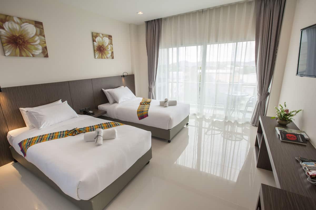 A hotel room with two beds, a desk, and a large window with curtains.