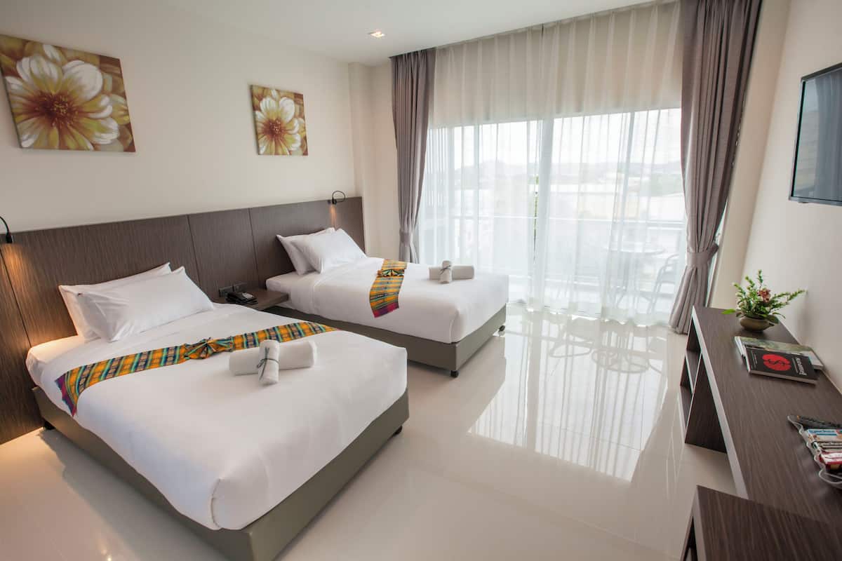 A hotel room with two beds, a desk, and a large window with curtains.