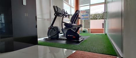 A hallway with a treadmill and a stationary bike, a red mat, and a green artificial turf area.