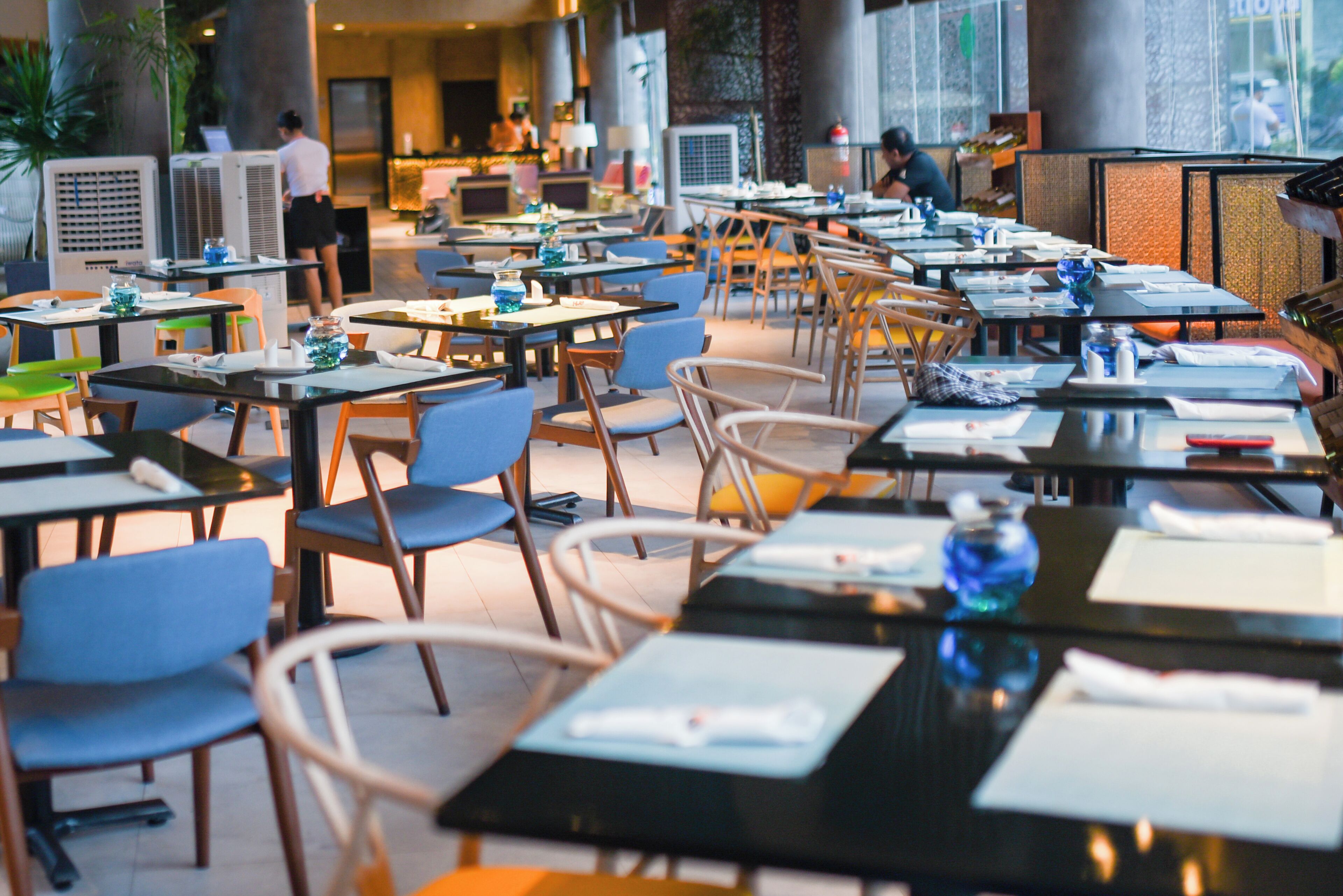 A spacious dining area with multiple tables and chairs, air conditioning units, and a view of the street outside.