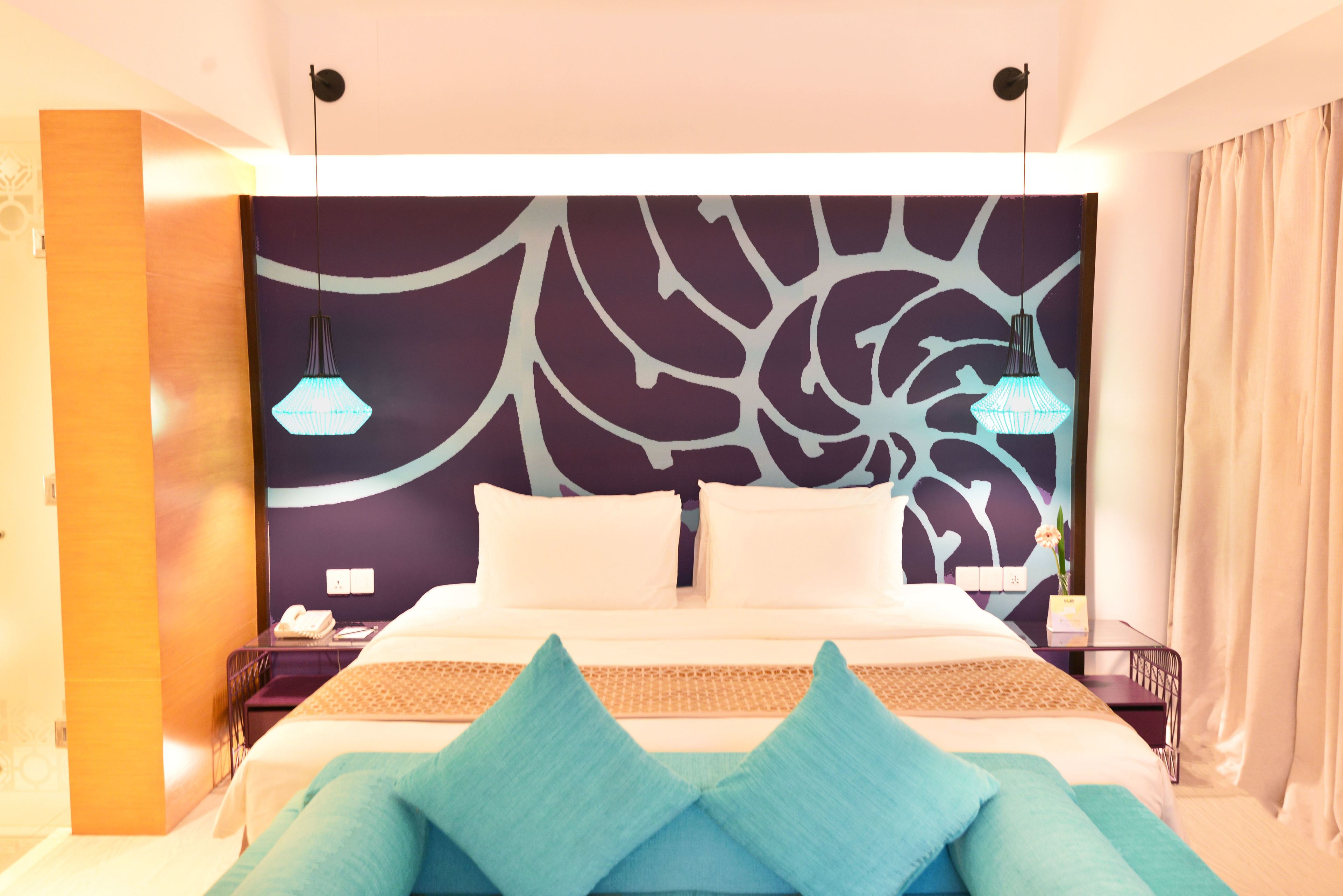 Quarto de hotel moderno com uma cama grande, duas mesas de cabeceira e uma parede decorativa com padrão de folha.