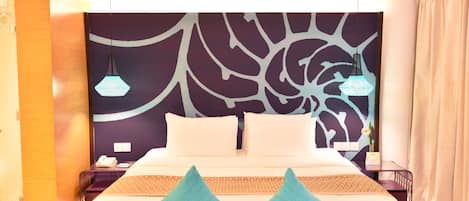 Quarto de hotel moderno com uma cama grande, duas mesas de cabeceira e uma parede decorativa com padrão de folha.